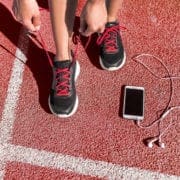 Runner tying shoes on red track beside smartphone