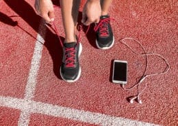 Runner tying shoes on red track beside smartphone