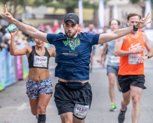 Runner excitedly crosses the 2019 Austin Half Marathon finish line. Run Austin, the #1 city in America and you will understand why people love the Austin Marathon!