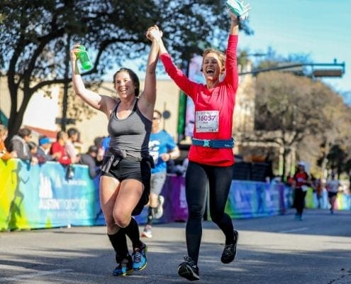Friend crossing the Austin Half Marathon finish line together; accountability is a great tip to stay motivated.