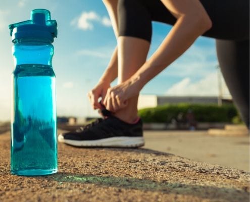 Image of runner tying her shoe with a water bottle nearby. Christy Thomas began running because she wanted to make a lifestyle change. She will run the 2020 Austin Half Marathon!