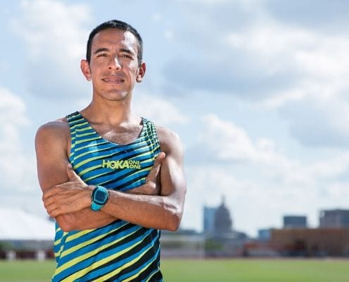 Leo Manzano, Austin Marathon Race Ambassador and Olympic silver medalist, poses on the University of Texas track with downtown Austin in the background. Manzano takes you back to his first sub-four-minute mile in this blog post.