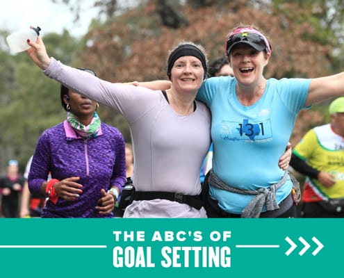 Two women happily stand side-by-side with their arms in the air during the 2020 Ascension Seton Austin Marathon. Text on design reads The ABCs of Goal Setting. Learn more at http://48d.435.myftpupload.com/goal-setting/
