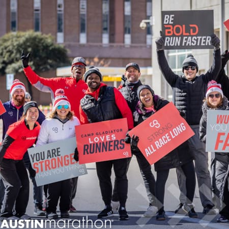 Group of Camp Gladiator coaches cheer for runners and hold signs. They were one of many local businesses to sponsor aid stations at a previous Austin Marathon. Learn more at https://youraustinmarathon.com/sponsor-aid-stations/