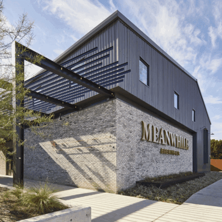 Modern gray brick and metal building with "Meanwhile Brewing Co." sign on the corner, black metal beams overhead, landscaped greenery, and a sidewalk under a partly cloudy sky—a standout among local Austin breweries. Austin Marathon Half Marathon & 5K Modern gray brick and metal building with "Meanwhile Brewing Co." sign on the corner, black metal beams overhead, landscaped greenery, and a sidewalk under a partly cloudy sky—a standout among local Austin breweries. Austin Marathon Half Marathon & 5K