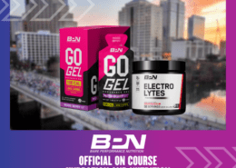 Image of two Bare Performance Nutrition products with a cityscape background. The products, "Go Gel, Mixed Berry" in a pink and black box and "Electrolytes" in a black tub, are showcased. Text below reads: "BPN - Official On-Course Hydration and Nutrition for the Ascension Seton Austin Marathon. Austin Marathon Half Marathon & 5K