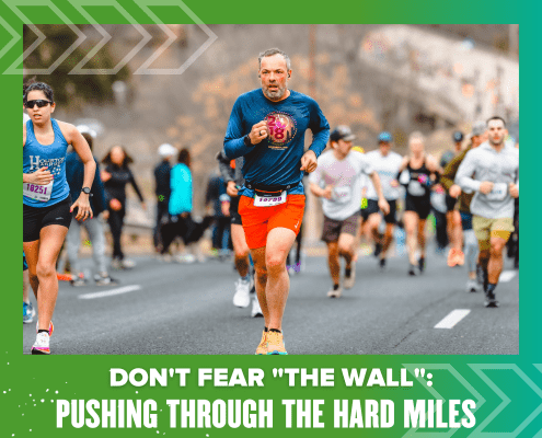 A group of runners participating in a marathon on a paved road, with the main focus on a middle-aged man in a blue long-sleeve shirt and red shorts. The image has a green border with the text "DON'T FEAR 'THE WALL'; PUSHING THROUGH THE HARD MILES" at the bottom. Austin Marathon Half Marathon & 5K