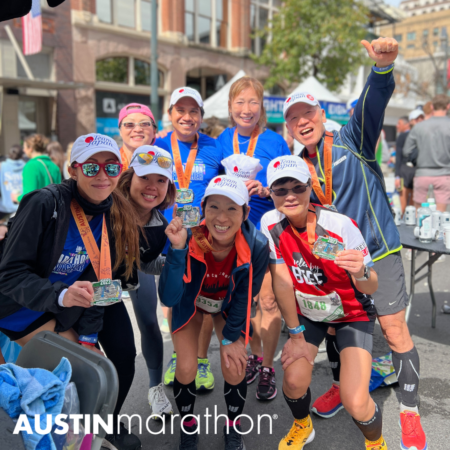 A group of smiling marathon runners proudly show their medals after completing the Austin Marathon. They are standing together in a celebratory pose, wearing athletic gear and caps. The background features event tents and spectators, debunking any myths about the difficulty of running such a race. The Austin Marathon logo is visible at the bottom. Austin Marathon Half Marathon & 5K