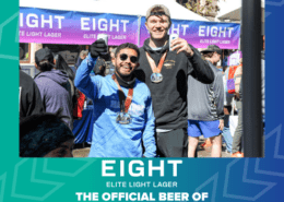 Two men wearing marathon medals stand smiling in front of a vendor backdrop for EIGHT Beer. They are posing happily, one holding a drink and giving a thumbs-up. The text reads, "The Official Beer of Austin Marathon," celebrating the exciting partnership. Austin Marathon Half Marathon & 5K