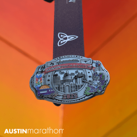 Close-up of the "Austin Marathon 2025" finisher medal featuring colorful images of buildings, a taco truck, and nature motifs. Race bling hangs from an attached ribbon against a gradient orange-yellow background. Text reads "AUSTINmarathon" at the bottom left. Austin Marathon Half Marathon & 5K