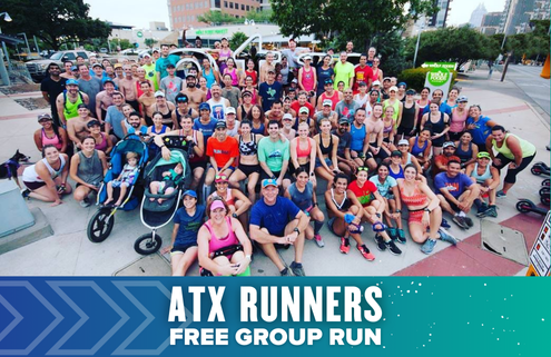 A large, diverse group of people poses together outdoors for a group photo after a run. Smiling in athletic wear, they stand behind a banner that reads "ATX Runners Free Group Run" celebrating their passion to Run Austin with blue and teal graphics. Austin Marathon Half Marathon & 5K