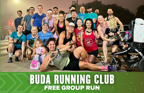 A diverse group of smiling people pose together outdoors before a run, some kneeling and others standing. Text at the bottom reads, "BUDA RUNNING CLUB FREE GROUP RUN" on a green banner, celebrating the spirit of the Austin International Half. Austin Marathon Half Marathon & 5K