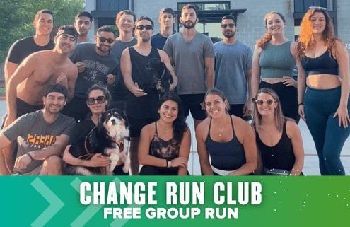 A group of 17 smiling people, some holding dogs, pose together outdoors in athletic wear after the Austin International Half. A green banner at the bottom reads “CHANGE RUN CLUB FREE GROUP RUN.”. Austin Marathon Half Marathon & 5K