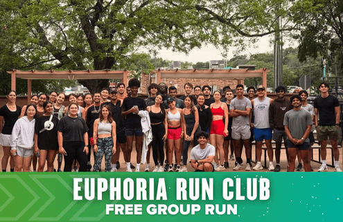 A large, diverse group of people in athletic wear stands together outdoors, smiling for a group photo during Launch Week. In front, a green banner reads, “EUPHORIA RUN CLUB FREE GROUP RUN.” Trees and street can be seen in the background. Austin Marathon Half Marathon & 5K