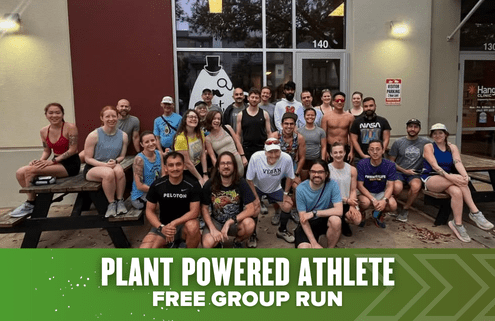 A large group of smiling people in athletic wear pose outside a building. Green text at the bottom reads "PLANT POWERED ATHLETE FREE GROUP RUN." The group looks ready for Run Austin or celebrating after the Austin Marathon. Austin Marathon Half Marathon & 5K