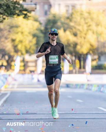 A runner sporting a black outfit and green shoes nears the Austin Marathon finish line, surrounded by colorful confetti and trees—the perfect moment for personal, official race photos. Austin Marathon Half Marathon & 5K