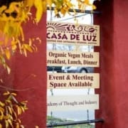 Wooden signs hanging on a red stucco wall, under yellow leaves, read: “Casa de Luz,” “Organic Vegan Meals Breakfast, Lunch, Dinner,” and more—perfect for those seeking Austin healthy dining or runner friendly restaurants. Austin Marathon Half Marathon & 5K