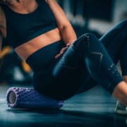 A person in athletic clothing uses a textured foam roller under their hip on a gym floor, highlighting post-exercise muscle recovery—an essential part of any beginner runner checklist. Austin Marathon Half Marathon & 5K