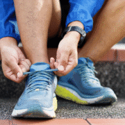 Close-up of a person sitting on outdoor steps, wearing blue athletic shoes and a smartwatch, tying the laces—a great visual for any beginner runner looking for running tips. The athlete is dressed in blue sportswear. Austin Marathon Half Marathon & 5K