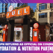 A BPN Fuel hydration and nutrition station with bright orange signage is set up outdoors in a city for the Ascension Seton Austin Marathon. Text below reads: "BPN returns as official on course hydration & nutrition partner. Austin Marathon Half Marathon & 5K