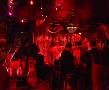 A dimly lit bar, one of the best spots Austin offers, with people seated at tables watching a live band perform on a stage decorated with red lights and shiny curtains, creating a cozy, vibrant atmosphere. Austin Marathon Half Marathon & 5K