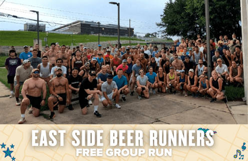 A large group of people pose outdoors for a group photo before a free group run, with greenery and a building in the background. The text overlay reads: "East Side Beer Runners Free Group Run. Austin Marathon Half Marathon & 5K