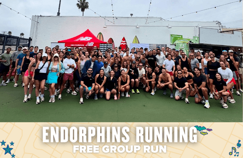 A large, diverse group of people in sporty attire smile and pose outdoors in front of surfboards and shops. A banner at the bottom reads "Endorphins Running Free Group Run," celebrating their energizing group run. Austin Marathon Half Marathon & 5K