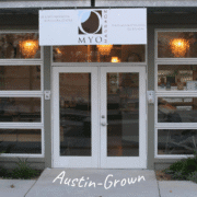 Glass storefront of MYO Massage, Austin’s Massage & Bodywork Center. A white sign with the business name and contact info hangs above the entrance. A hidden gem in Austin, perfect for post-run recovery. The words “Austin-Grown” appear at the bottom. Austin Marathon Half Marathon & 5K