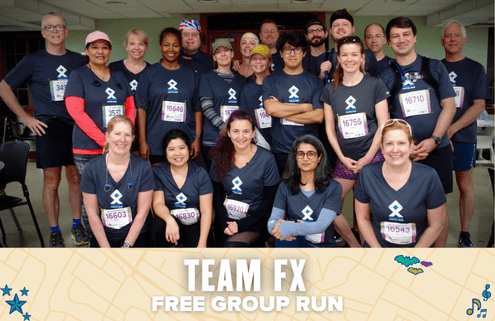 A group of 20 people wearing matching "Team FX" shirts and race bibs pose indoors, smiling for a group photo. A banner at the bottom reads: "TEAM FX FREE GROUP RUN," highlighting their fun group run event with decorative graphics. Austin Marathon Half Marathon & 5K