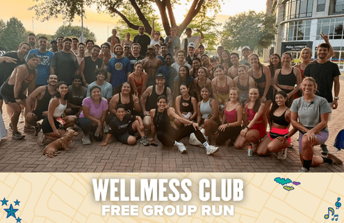 A large, diverse group of people pose and smile together outdoors after a Wellmess Club free group run, with a small dog at the front. Text at the bottom reads, "WELLMESS CLUB FREE GROUP RUN. Austin Marathon Half Marathon & 5K