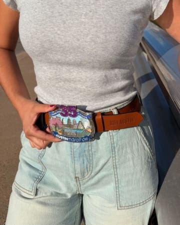 A person wearing light denim shorts and a gray T-shirt displays a large, colorful "35th Austin Marathon" race bling belt buckle and a brown belt with "RUN AUSTIN" embossed on it. Austin Marathon Half Marathon & 5K A person wearing light denim shorts and a gray T-shirt displays a large, colorful "35th Austin Marathon" race bling belt buckle and a brown belt with "RUN AUSTIN" embossed on it. Austin Marathon Half Marathon & 5K