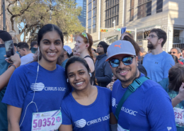 Three runners in blue shirts smiling at race