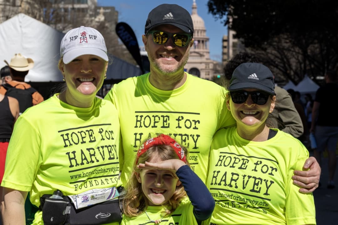 Four people wearing bright yellow "Hope for Harvey" shirts pose and smile outdoors at a Charity Teams fundraising event. A child stands in front, making a hand gesture, with the Texas Capitol visible in the background. Austin Marathon Half Marathon & 5K Four people wearing bright yellow "Hope for Harvey" shirts pose and smile outdoors at a Charity Teams fundraising event. A child stands in front, making a hand gesture, with the Texas Capitol visible in the background. Austin Marathon Half Marathon & 5K