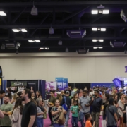 A large crowd of people walk and gather at an indoor expo or convention, surrounded by vendor booths and colorful banners under bright overhead lights—an exciting opportunity to become a sponsor and boost your brand’s visibility. Austin Marathon Half Marathon & 5K