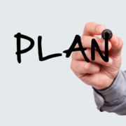 A hand holding a black marker writes the word "PLAN" in large, bold letters on a transparent surface against a light gray background, reminding us to plan ahead for when motivation fades. Austin Marathon Half Marathon & 5K