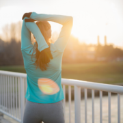 A person in athletic clothing stretches their arms overhead while standing on a bridge at sunrise, embodying the energy needed when motivation fades. The sun shines brightly in the background as they face away from the camera. Austin Marathon Half Marathon & 5K