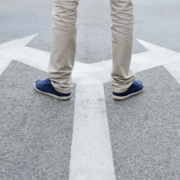 A person wearing beige pants and blue shoes stands on a road where large white arrows point in different directions, reminding us that when motivation fades, choices still await to guide our next steps. Austin Marathon Half Marathon & 5K