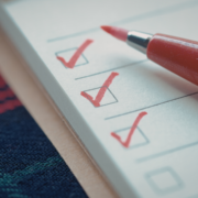 A close-up of a checklist with three boxes ticked in red ink, next to a red marker pen—capturing the moment before motivation fades. The background includes a multicolored fabric and part of a beige surface. Austin Marathon Half Marathon & 5K