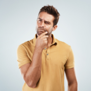 A man in a yellow polo shirt stands against a light background, touching his chin and squinting with a thoughtful, puzzled expression—perhaps pondering how to build running endurance or avoid burnout. Austin Marathon Half Marathon & 5K