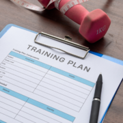 A clipboard with a “TRAINING PLAN” form, a black pen, a pink 1kg dumbbell, and a measuring tape—essential tools for effective time management and February planning—all thoughtfully arranged on a wooden surface. Austin Marathon Half Marathon & 5K