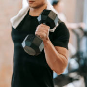 A person in a black shirt holds a dumbbell in one hand and has a white towel draped over their neck, working out in a gym, embodying top productivity tips for effective time management and February planning. Austin Marathon Half Marathon & 5K