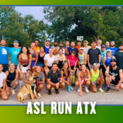 A large group of people and a dog pose outdoors in athletic wear, smiling for a group photo before a Group Run. The bottom of the image reads “ASL RUN ATX” with blue bat silhouettes in the corners. Austin Marathon Half Marathon & 5K