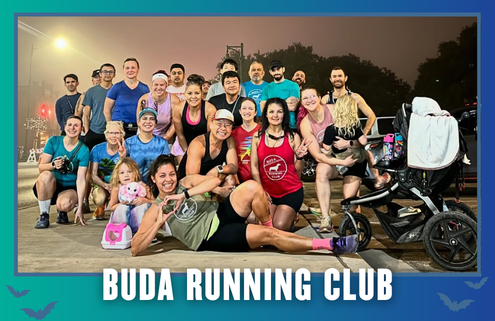 A diverse group of people, including kids and a dog, pose smiling in athletic wear on a sidewalk at dawn with streetlights, ready for their South Austin group run. The text below reads “BUDA RUNNING CLUB.”. Austin Marathon Half Marathon & 5K
