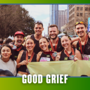A group of smiling marathon runners with medals pose together outdoors in a city, holding a yellow banner for their KickOff Week. Text at the bottom reads “GOOD GRIEF.” Buildings and trees are visible in the background. Austin Marathon Half Marathon & 5K