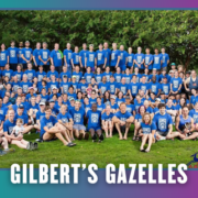 A large group of people wearing matching blue shirts sits and stands together outdoors on grass, smiling at the camera during a Group Run. The text “GILBERT’S GAZELLES” is displayed at the bottom of the image. Austin Marathon Half Marathon & 5K