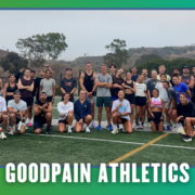 A large group of people in athletic wear poses together on a sports field with hills in the background, celebrating their group run for ATX KickOff Week. The text “GOODPAIN ATHLETICS” is displayed at the bottom of the image. Austin Marathon Half Marathon & 5K