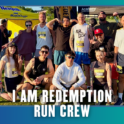 A group of 13 smiling runners in athletic gear pose together outdoors after a race in South Austin. Some wear medals and bib numbers, celebrating their accomplishment. The words “I AM REDEMPTION RUN CREW” are displayed at the bottom, capturing the spirit of this vibrant Group Run. Austin Marathon Half Marathon & 5K