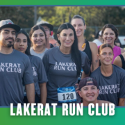 A group of smiling people wearing “Lakerat Run Club” shirts pose together outdoors at a South Austin running event during KickOff Week, with trees in the background and race numbers visible, celebrating their group run. Austin Marathon Half Marathon & 5K