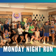 A group of people in athletic wear pose together indoors, smiling and ready for a group run. Text at the bottom reads “Monday Night Run.” The background displays hats and clothing on the walls, hinting at the community spirit of Lakerat Run Club as they celebrate KickOff Week. Austin Marathon Half Marathon & 5K