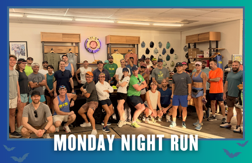 A group of people in athletic wear pose together indoors, smiling and ready for a group run. Text at the bottom reads “Monday Night Run.” The background displays hats and clothing on the walls, hinting at the community spirit of Lakerat Run Club as they celebrate KickOff Week. Austin Marathon Half Marathon & 5K